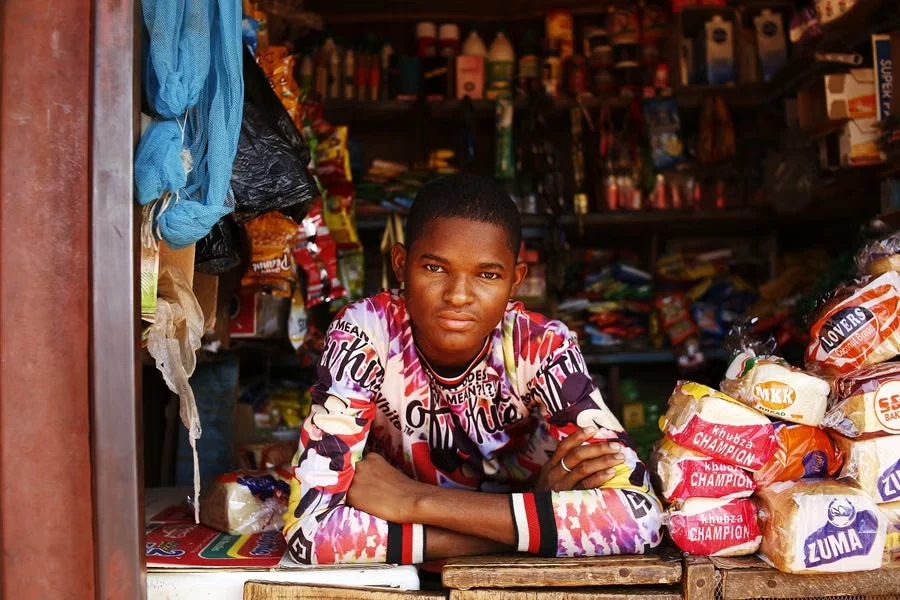 A shop owner leaning on the counter of a well-stocked general store